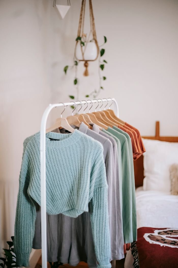 Interior of light bedroom with collection of trendy clothes on hangers near bed and white wall with potted plant